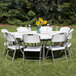 A Flash Furniture white plastic folding table set up with white folding chairs on grass.