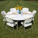 A Flash Furniture white plastic folding table set with white chairs and a vase of sunflowers on it.