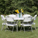 A white Flash Furniture round folding table set up on grass with white folding chairs.