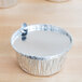 A round aluminum foil container with a foil board lid on a wooden table.