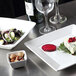 A Tuxton TuxTrendz bright white square china plate with food and a wine glass on a table.