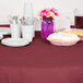 A table set with a burgundy Creative Converting tissue/poly table cover, plates, and utensils.