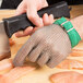 A person's hand wearing a Victorinox cut resistant chain mail glove while cutting meat.