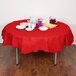 A table with a red Creative Converting tissue and poly table cover with plates and cups on it.