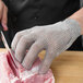 A person's hand wearing Victorinox stainless steel mesh gloves cutting meat.