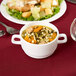 A bowl of soup with vegetables and bread in an Arcoroc white double handled bowl on a table.