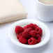 An Arcoroc white glass bowl filled with raspberries on a white background.