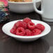 A white Arcoroc glass bowl filled with raspberries on a table.