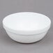 An Arcoroc white stacking bowl on a gray surface.