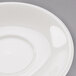 A Tuxton eggshell white saucer with a small rim on a gray surface.