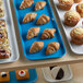 A blue Cambro market tray filled with pastries and muffins on a bakery display counter.