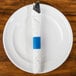 A fork and knife wrapped in a blue napkin with a blue napkin band.