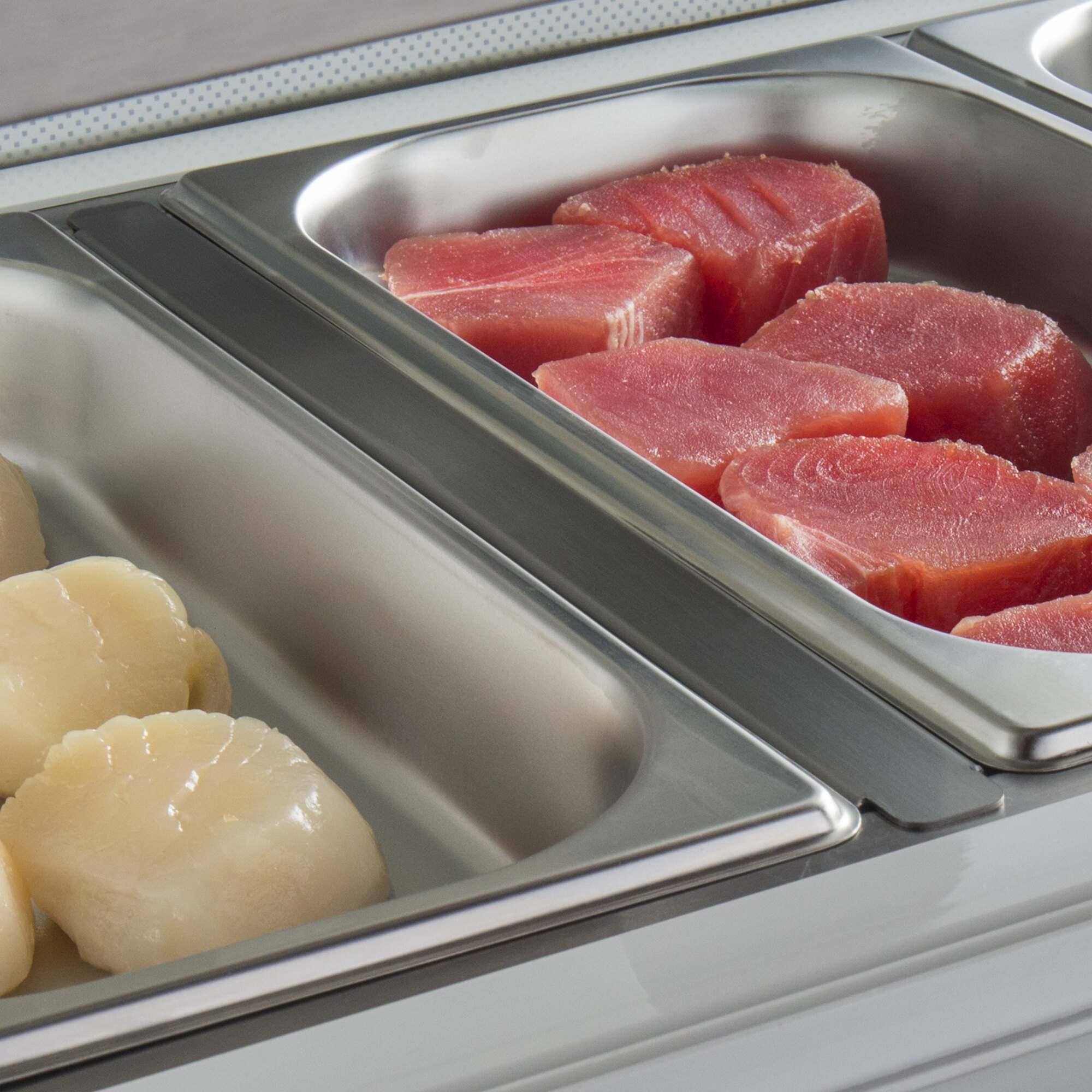A white hotel buffet tray with raw meat and scallops divided with an Avantco divider bar.