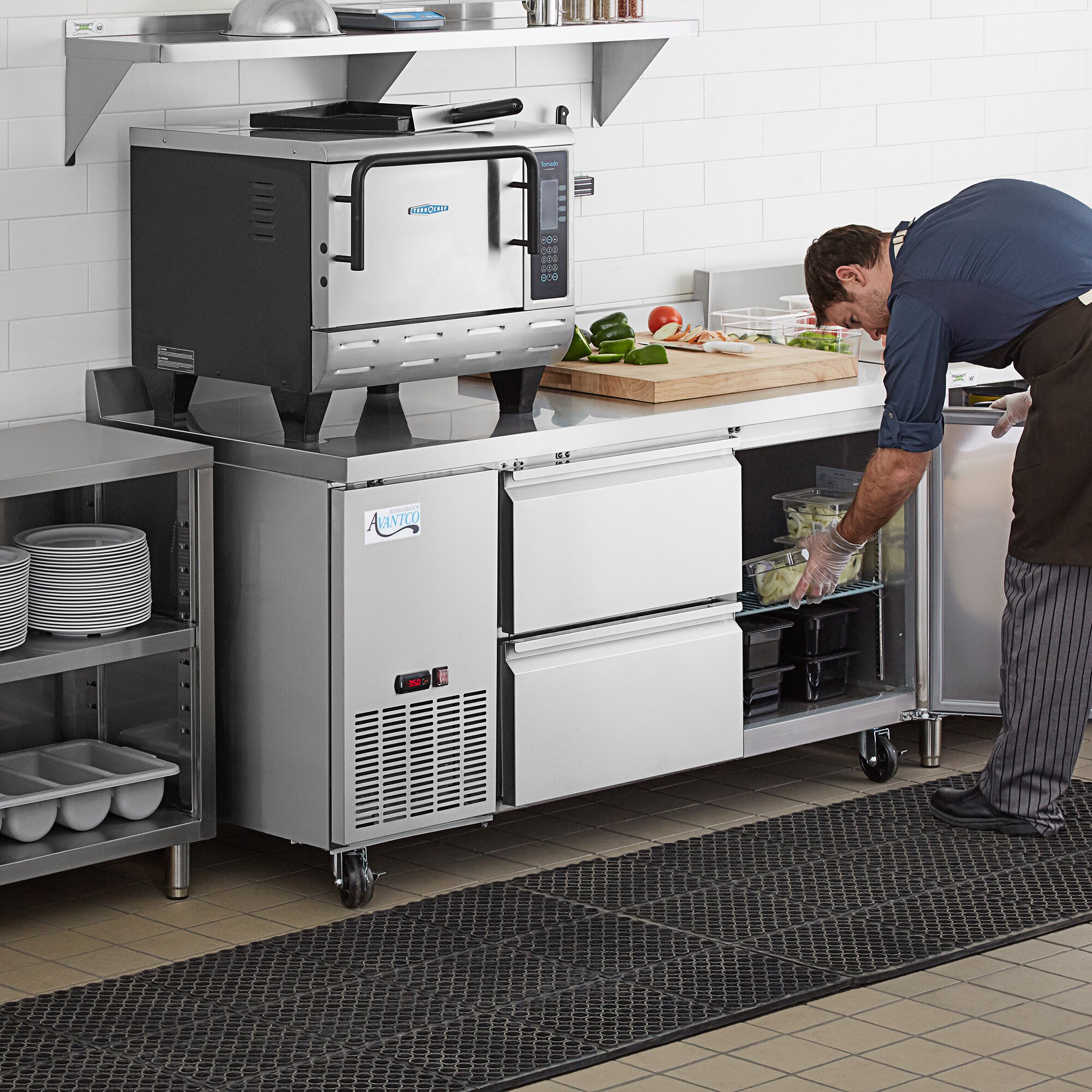A man using an Avantco stainless steel worktop refrigerator in a professional kitchen.