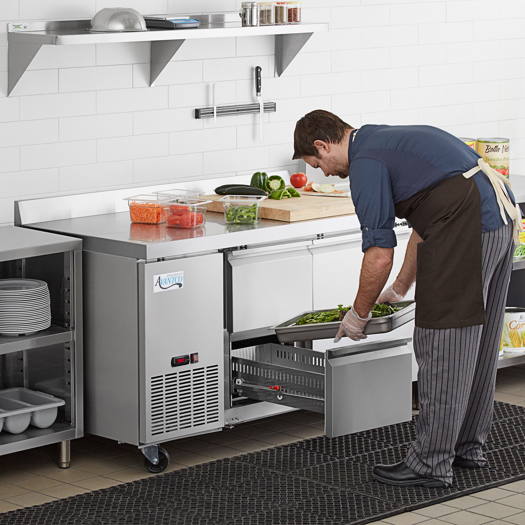 A man preparing food on an Avantco stainless steel worktop refrigerator with drawers.