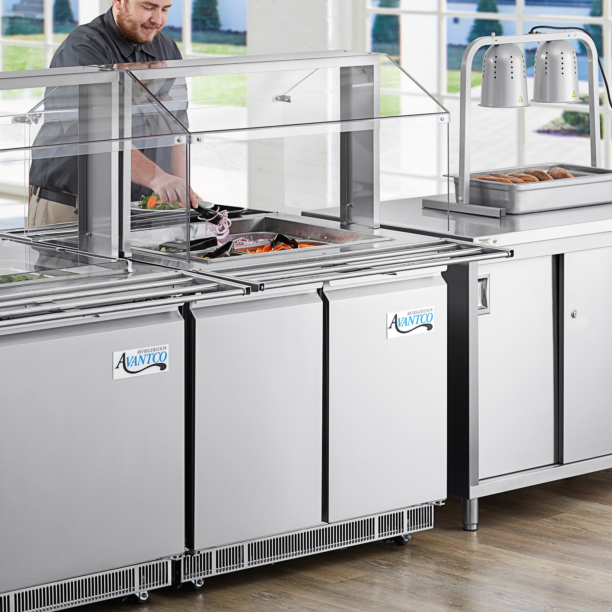 A man standing behind a white Avantco Sneeze Guard canopy on a refrigerated food table.