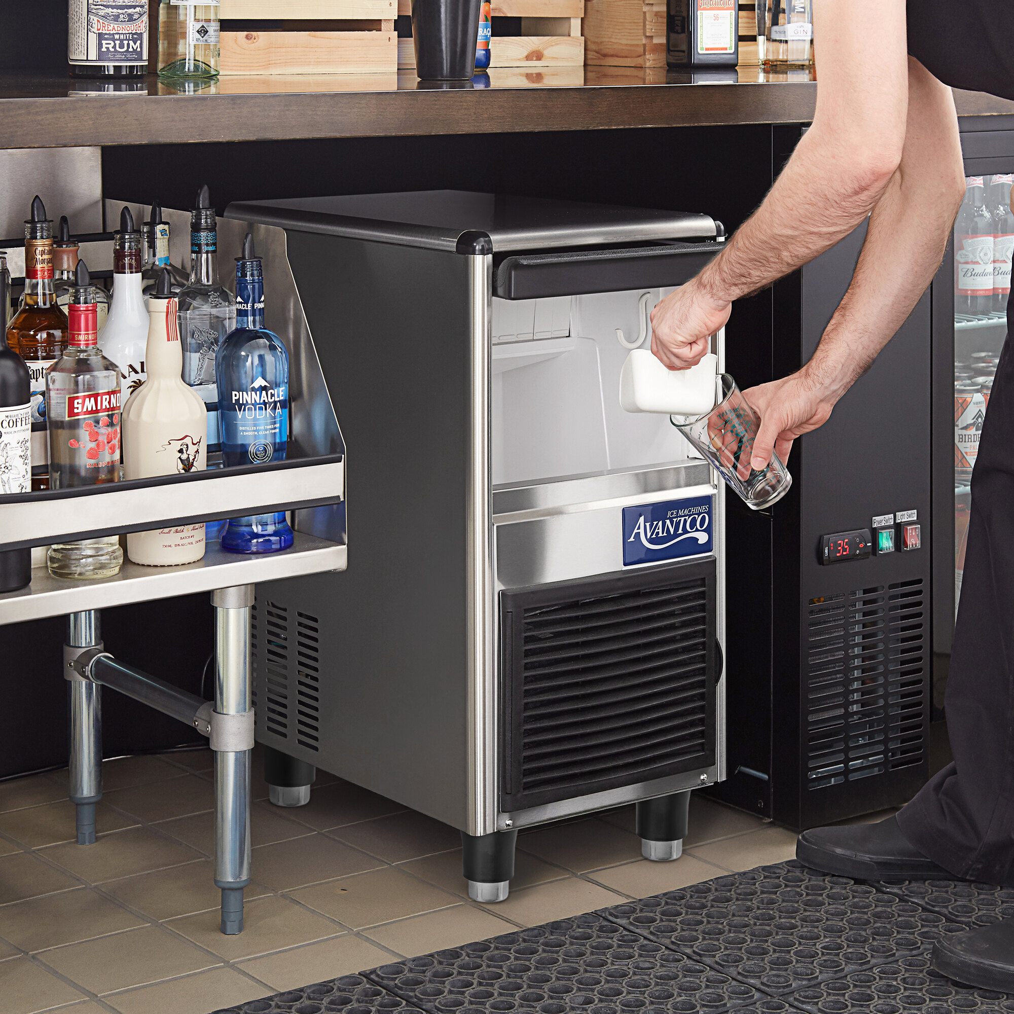 A man pouring a glass of ice from an Avantco undercounter ice machine.