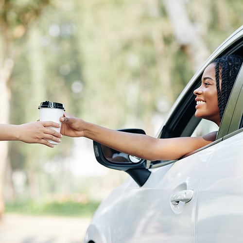 A.pretty young black woman smiles at a drive-thru worker while buying coffee from a drive through coffee shop