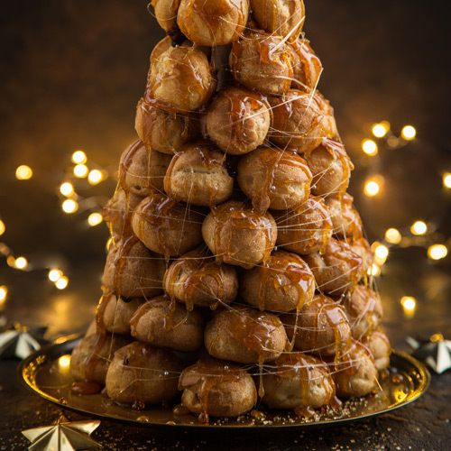 A croquembouche with white Christmas lights in the background.