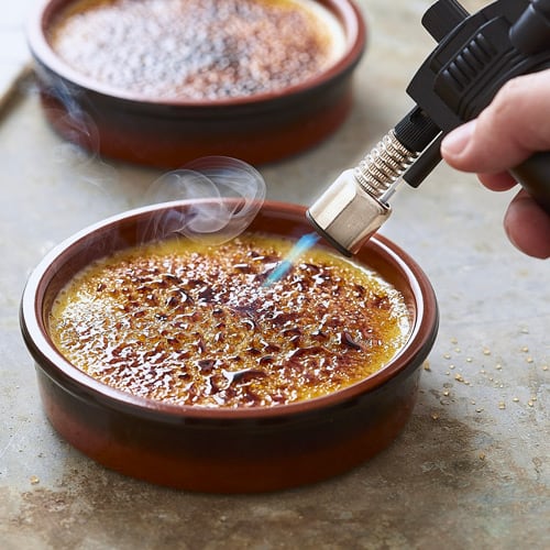 A cooking torch heating up the top of some flan.