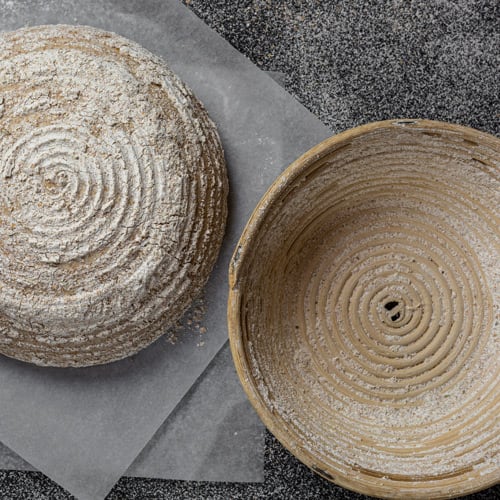 Two proofing baskets, one upright and one upside down on a counter.