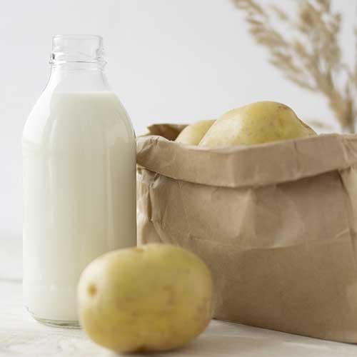 potato milk in a glass bottle on a white wooden background