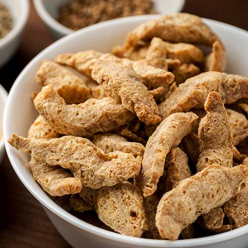 raw dry soya meat chunks in a white bowl on a wooden table with different spices