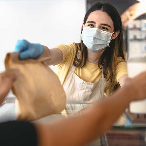 young woman worker wearing face mask giving takeout meal to customers