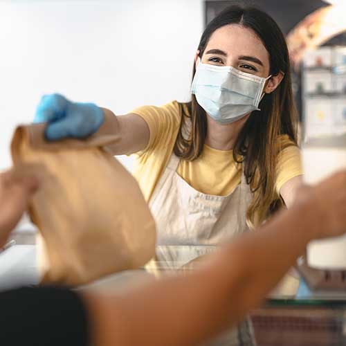 young woman worker wearing face mask giving takeout meal to customers