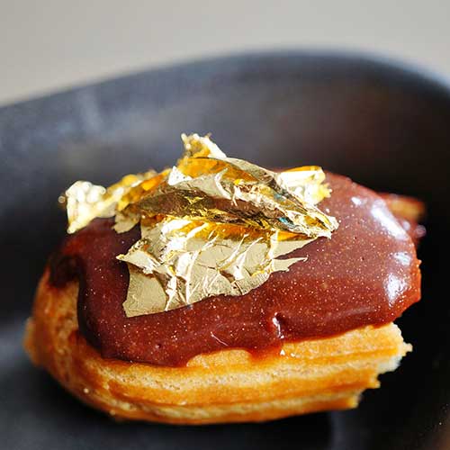 bite of a chocolate eclair pastry with an edible gold leaf on top