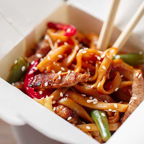 chow mein with pork and vegetables in take out box on wooden table