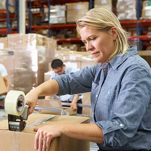 female warehouse worker sealing cardboard box with tape roll dispenser