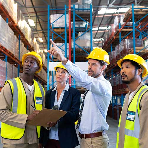 male supervisor standing with coworkers and pointing to something in the distance in warehouse