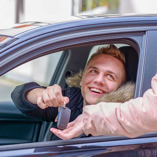 smiling young man in a car handing over his keys