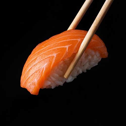 traditional japanese nigiri sushi with salmon placed between chopsticks