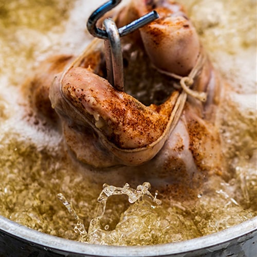 Turkey on a hook, partially submerged in boiling oil inside a deep fryer
