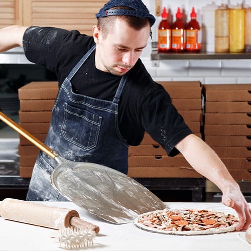 man sliding an uncooked pizza on to a pizza peel