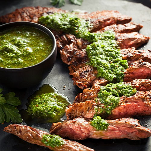 Strips of medium-rare steak drizzled in chimichurri sauce