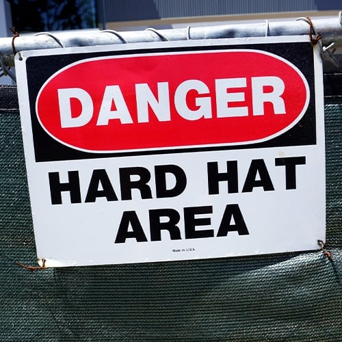 a safety sign on a fence that says DANGER hard hat area
