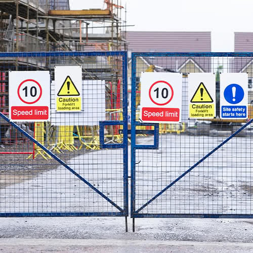  various safety signs on a metal fence barricading an industrial space