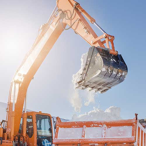 an excavator loads snow into a truck body