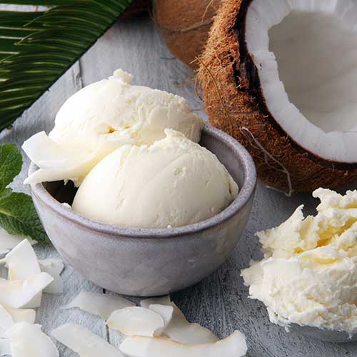 bowl with balls of coconut ice cream and pieces of coconut on wooden table