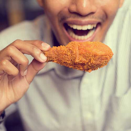 close up focus of man holding fried chicken drumstick