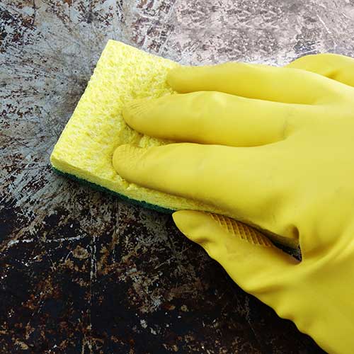 hand with yellow glove cleaning baking sheet with sponge