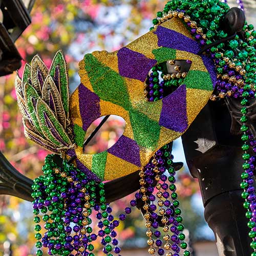 mardi gras beads and mask on light post outside in sunshine