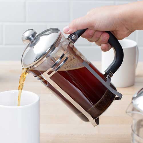 coffee being poured into a white mug out of a french press