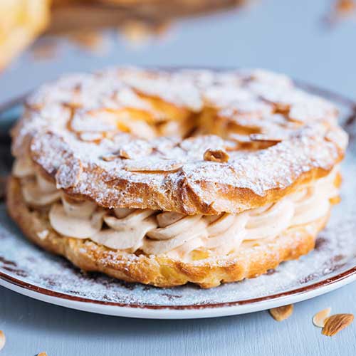 paris brest on a grey background with powdered sugar almond leaves and almond creme between