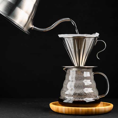 process of brewing coffee in pour over filter coffee through a glass coffee pot on a wooden tray