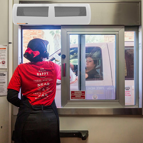 an air curtain on an open drive through window blows air while an employee hands a customer their order