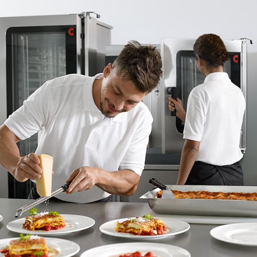 chef grating parmesan cheese over hot lasagna